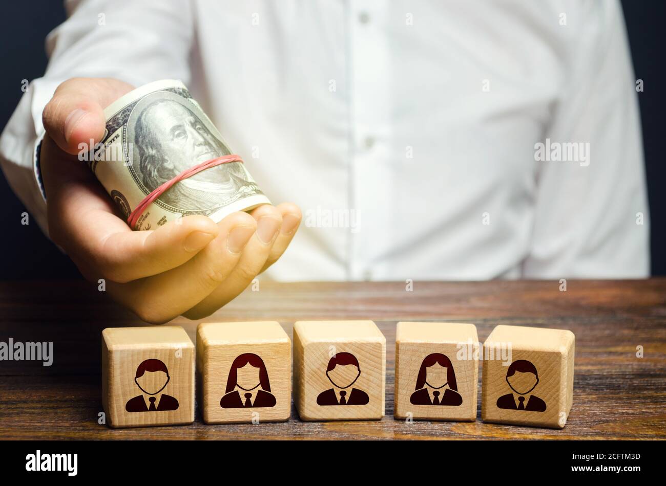 A man holds out money dollars over blocks with employees. Fair pay increase. Incentives for employees with bonuses. Investments. Company personnel cos Stock Photo