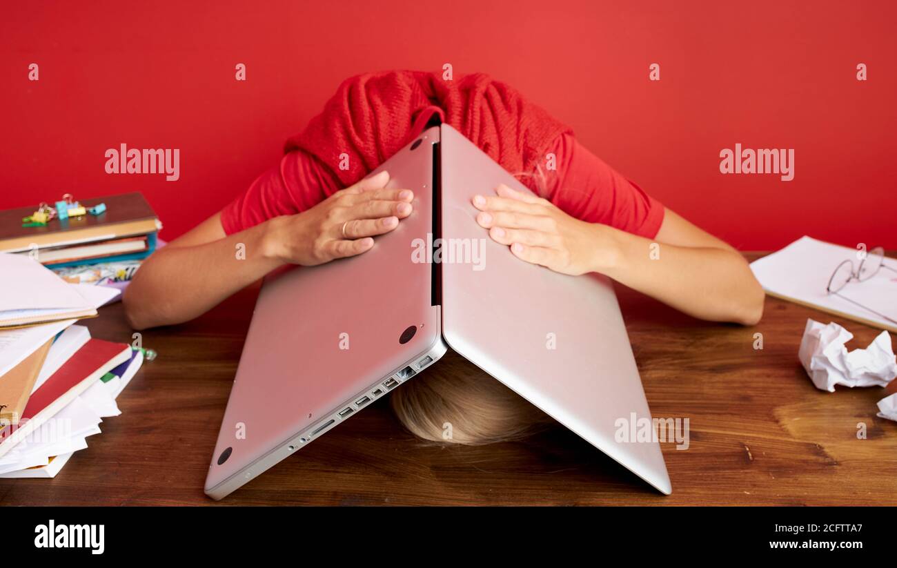 portrait of a young caucasian woman holding laptop computer on his head, deadline at work, frustration concept, being fired from job dismissed at work Stock Photo