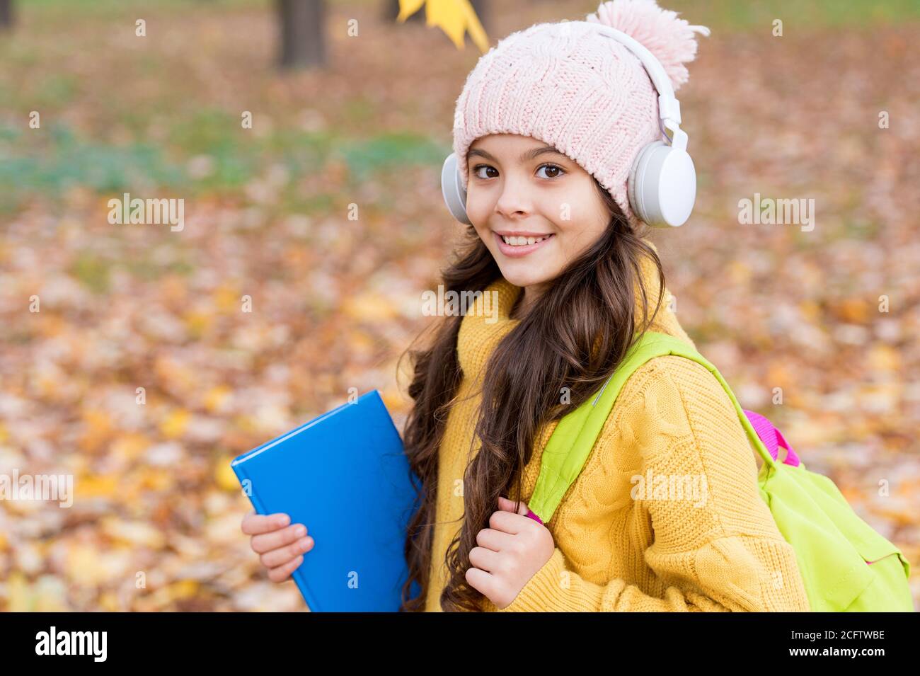 pupil in earpieces hold book while walking in park, education. Stock Photo