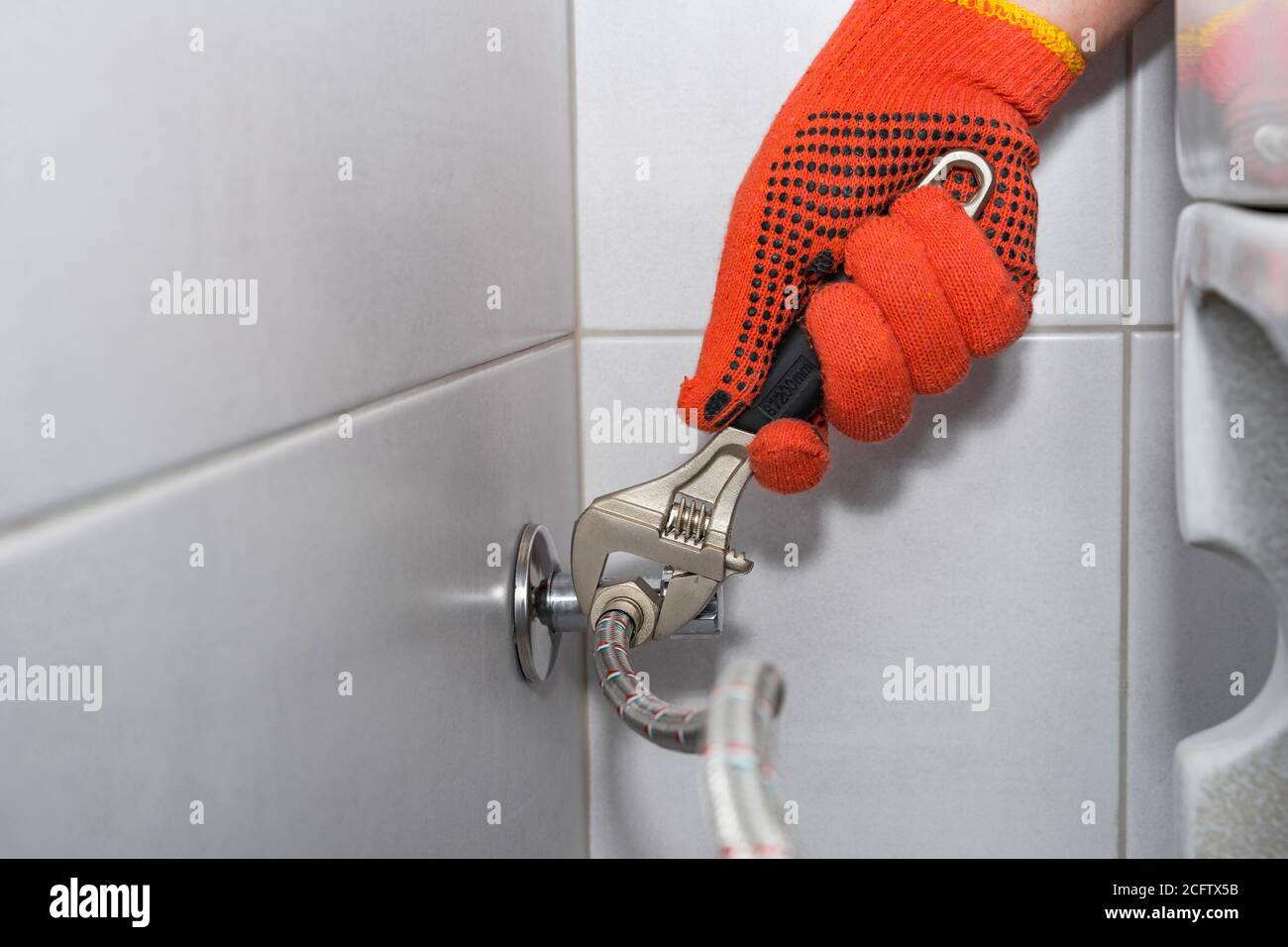 Plumber installs of a toilet hose in a hardtoreach place with an