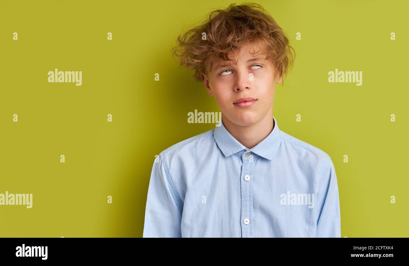 teen boy rolled his eyes, tired of listening to nonsense. caucasian boy in shirt with curly hair posing at camera isolated over green background Stock Photo