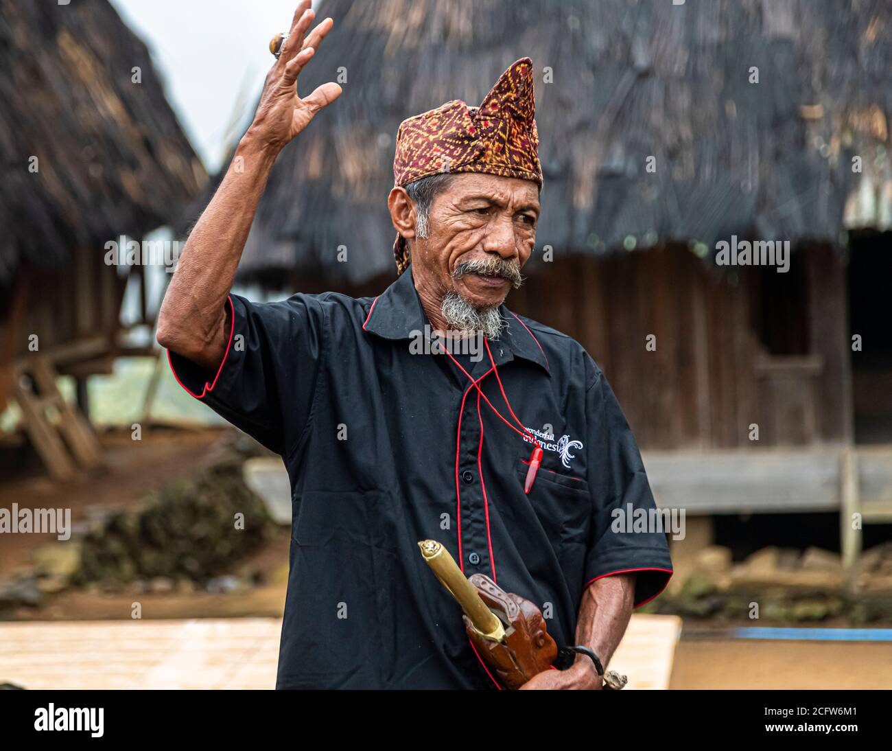 The village chief wears a pointed ikat headdress and gestures during his address in front of the thatched-roof houses of a mountain village near Moni, Flores, Indonesia. Stock Photo