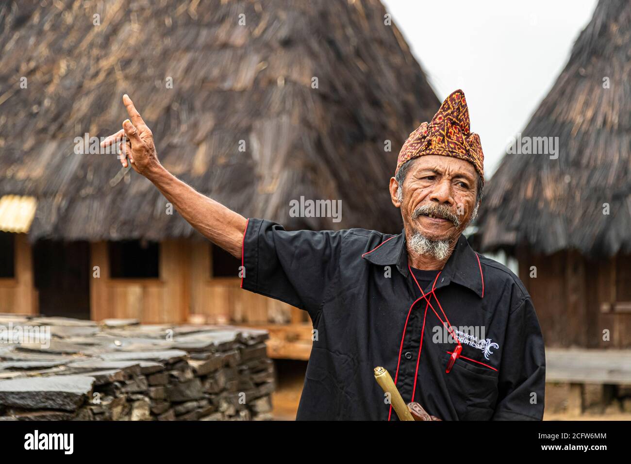 The village chief of a mountain village near Moni, Flores, Indonesia, stretches out his arm and points into the distance as he addresses visitors in front of the village's cone-roofed thatched houses. Stock Photo