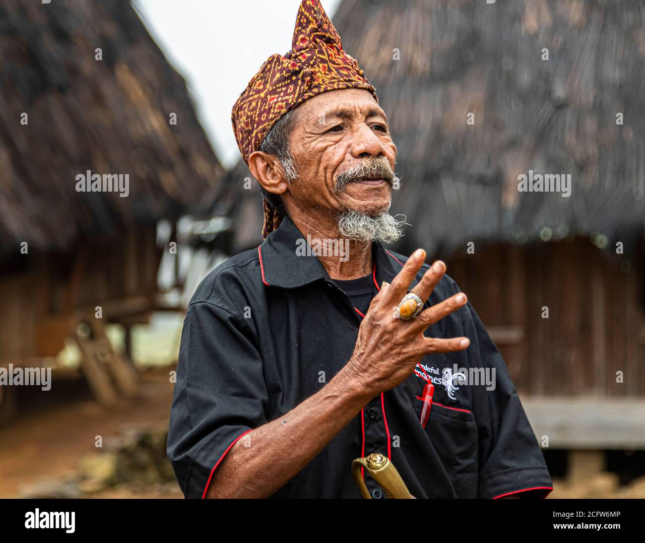 The village chief speaks in front of a traditional thatched-roof dwelling in a mountain village near Moni, Flores, Indonesia. Stock Photo