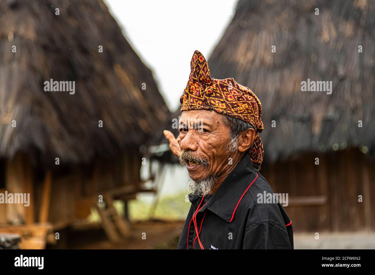 The village chief of a mountain village near Moni, Flores, Indonesia, speaks with his mouth open and glances to the side, his gesturing hand blurred in the background. Stock Photo