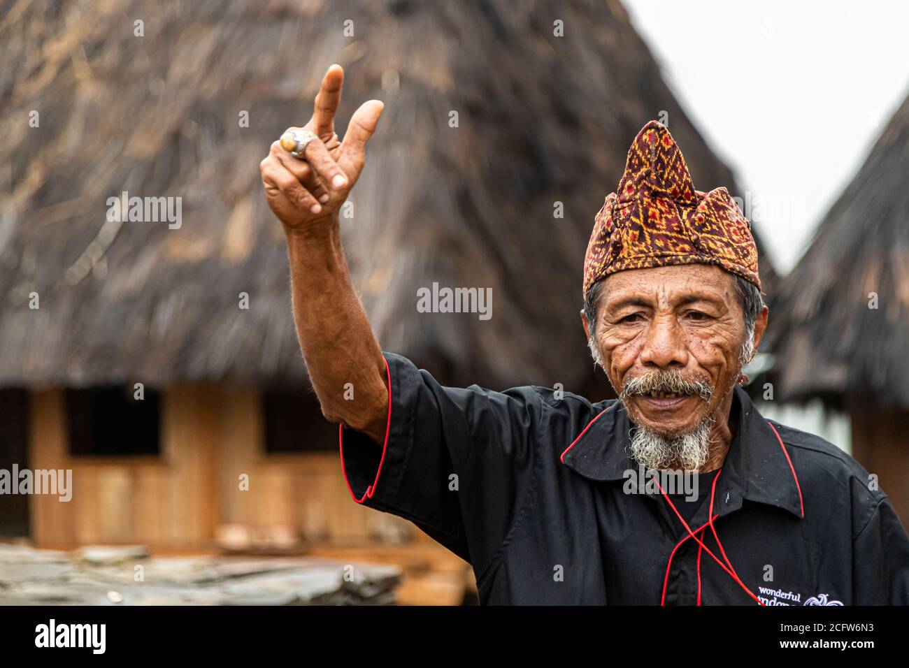 The village chief of a mountain village near Moni, Flores, Indonesia, raises two fingers of his lifted hand as he speaks to visitors with a serious expression. Stock Photo