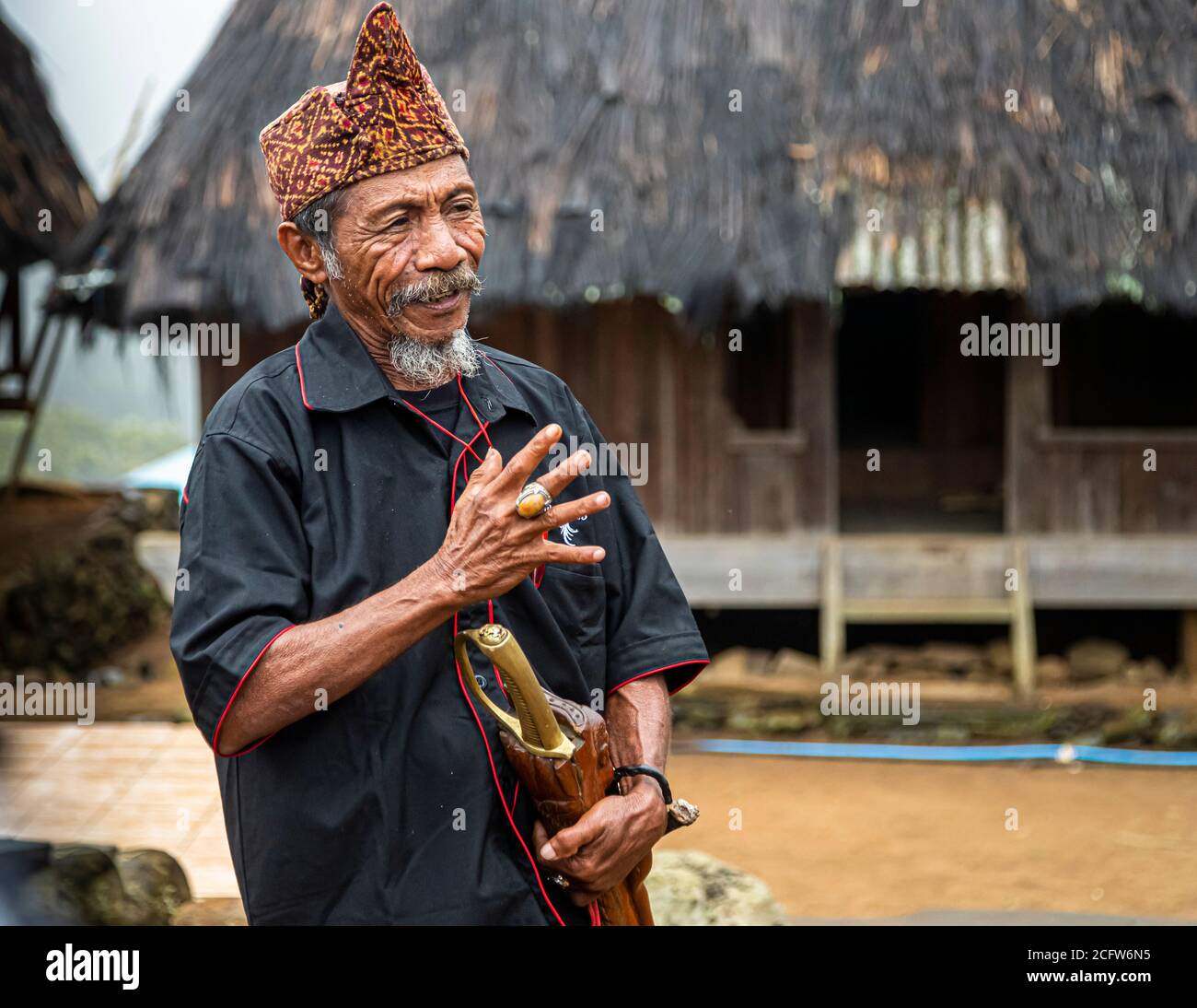 The village chief smiles during his address, a traditional dwelling in the background, mountain village near Moni, Flores, Indonesia. Stock Photo