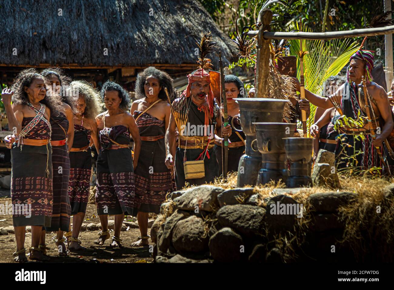 Women in dark ikat dress stand before the bronze Moko drums in the village of Takpala, Alor, Indonesia, old heirlooms traditionally used as bride price on Alor. Stock Photo