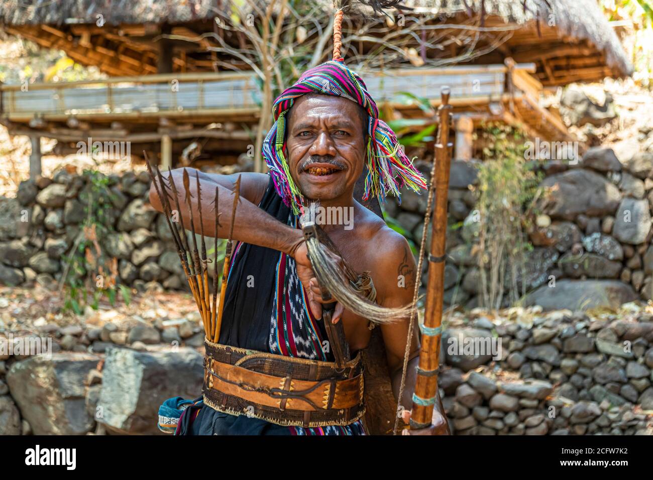 The warrior in a colourful headscarf, his teeth stained red from chewing betel nut, holds arrows, a bow and a machete, village of Takpala, Alor, Indonesia. Stock Photo