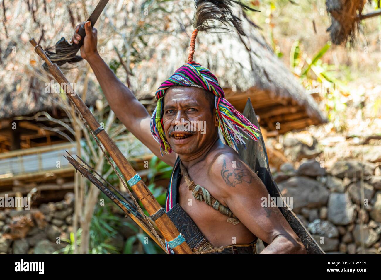 A tattooed warrior raises a machete above his head while holding a bow and arrows in his other hand, during the Lego-Lego dance in Takpala, Alor, Indonesia. Stock Photo