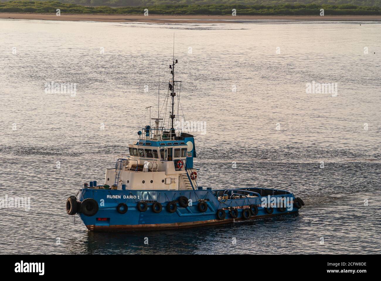 Corinto, Nicaragua - November 27, 2008: Blue and white Ruben Dario 1 tugboat and pilot outside the harbor on silver ocean water, with belt of green bo Stock Photo