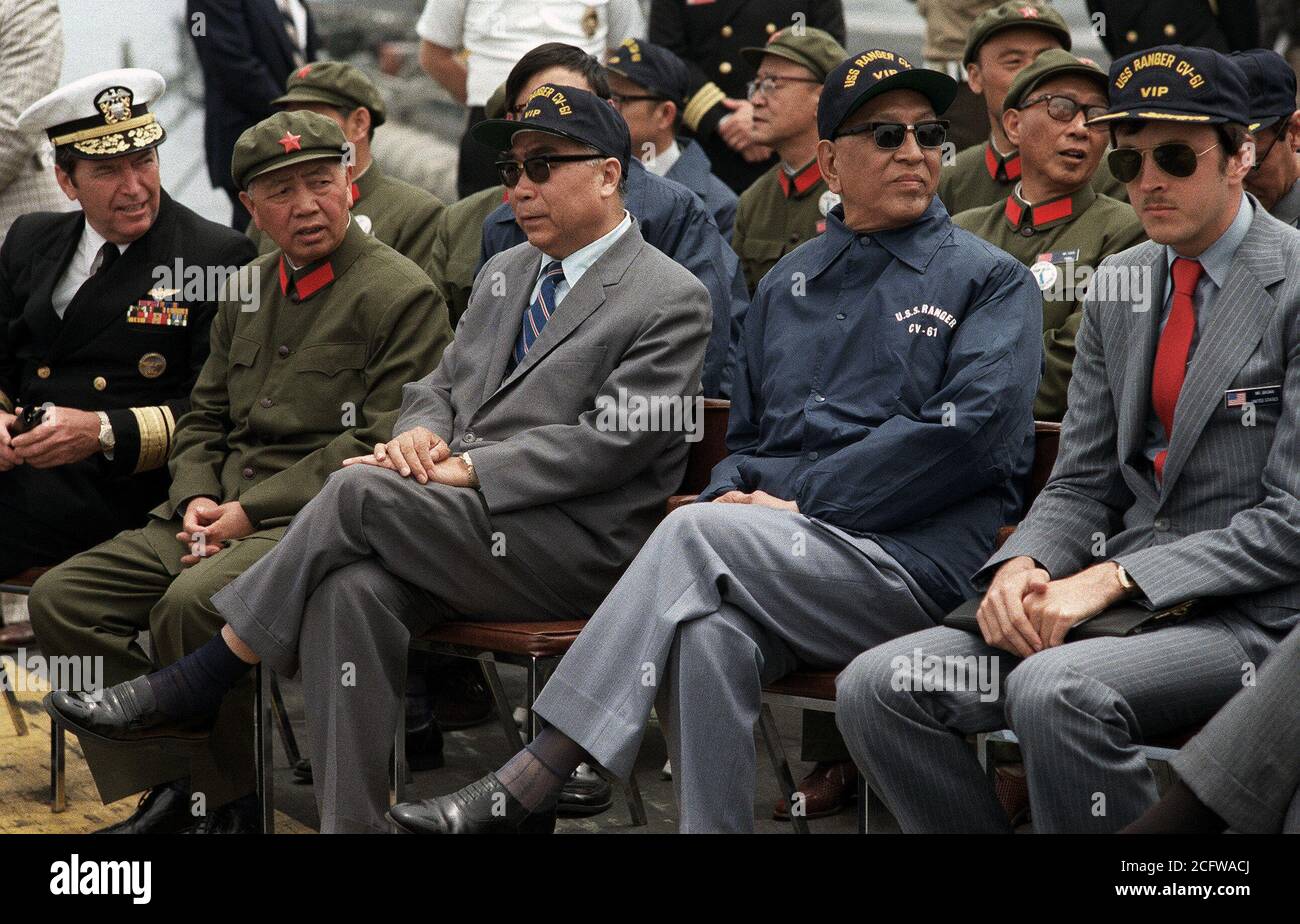 1980 - Vice Premier Geng Biao of China, in the blue jacket, and the Chinese ambassador sit with U.S. Navy officials aboard the aircraft carrier USS RANGER (CV-61).  They are waiting for the start of the air and sea demonstration. Stock Photo