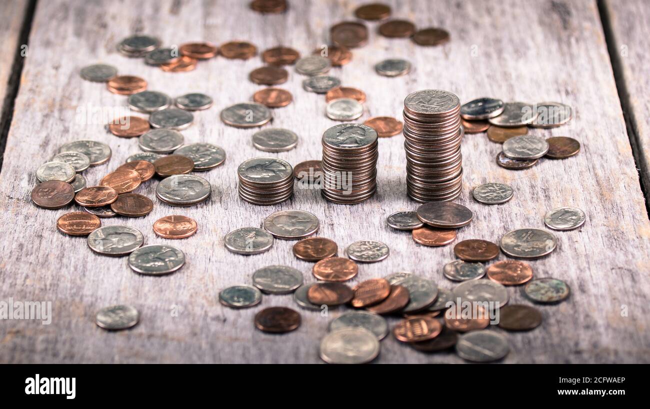 Stacks of quarters on an old wooden table amid scattered coins / investment growth concept Stock Photo