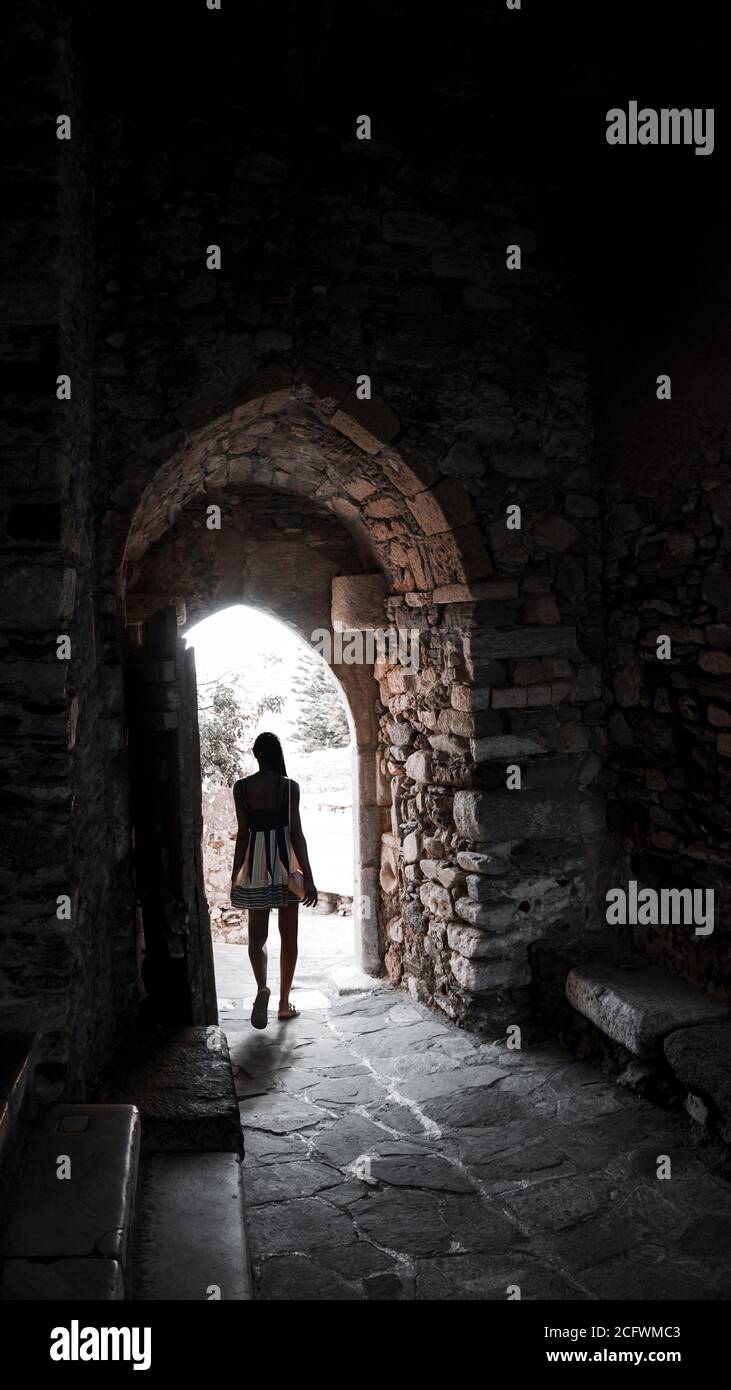 The girl travels alone to the ancient sights of the Greek islands. Arched street with a tunnel passage. Dark-skinned young attractive woman in backlig Stock Photo