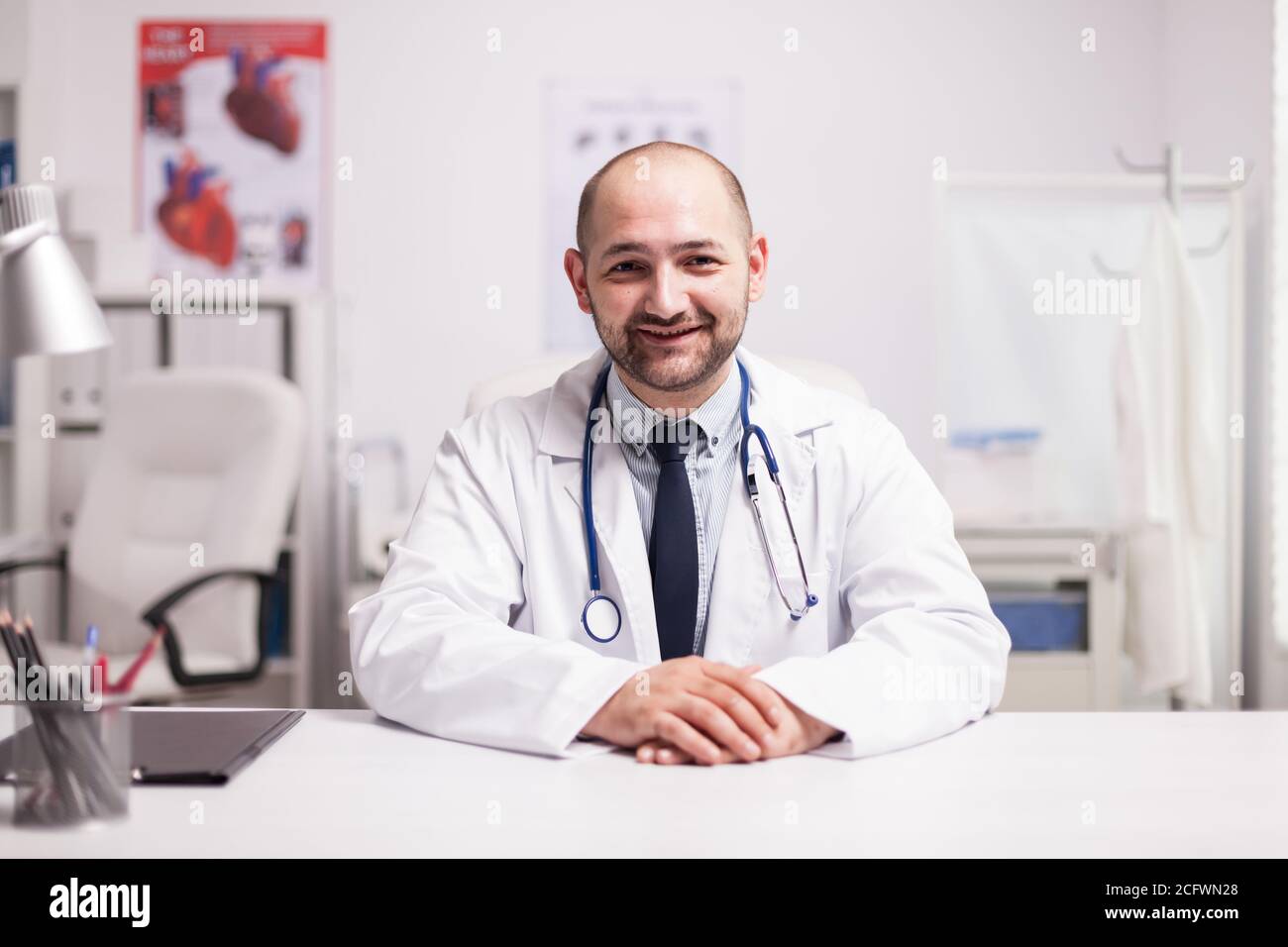 Portrait of young doctor smiling looking at the camera in hospital office wearing white coat and stethoscope. Stock Photo