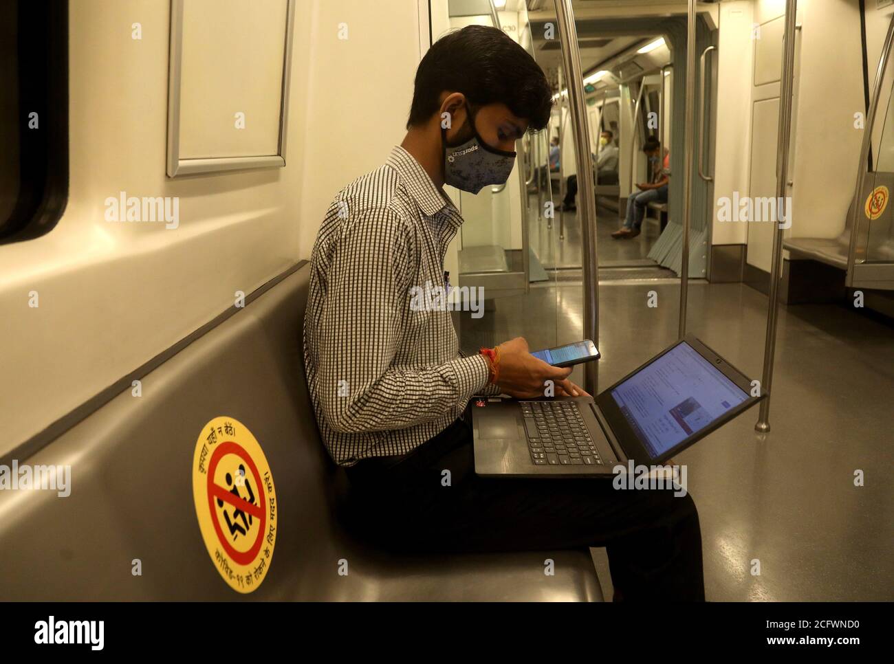 New Delhi, India. 07th Sep, 2020. A man is seen on his laptop and phone while wearing a facemask and observing social distance on the Delhi Metro on its first day of reopening after 5 months of lockdown due to Covid-19.On the first day, the yellow line between HUDA City Centre and Samaypur Badli, will run from 7 to 11 am, and 4 to 8 pm in the 2nd phase. The metro will resume full services from September 12. Credit: SOPA Images Limited/Alamy Live News Stock Photo