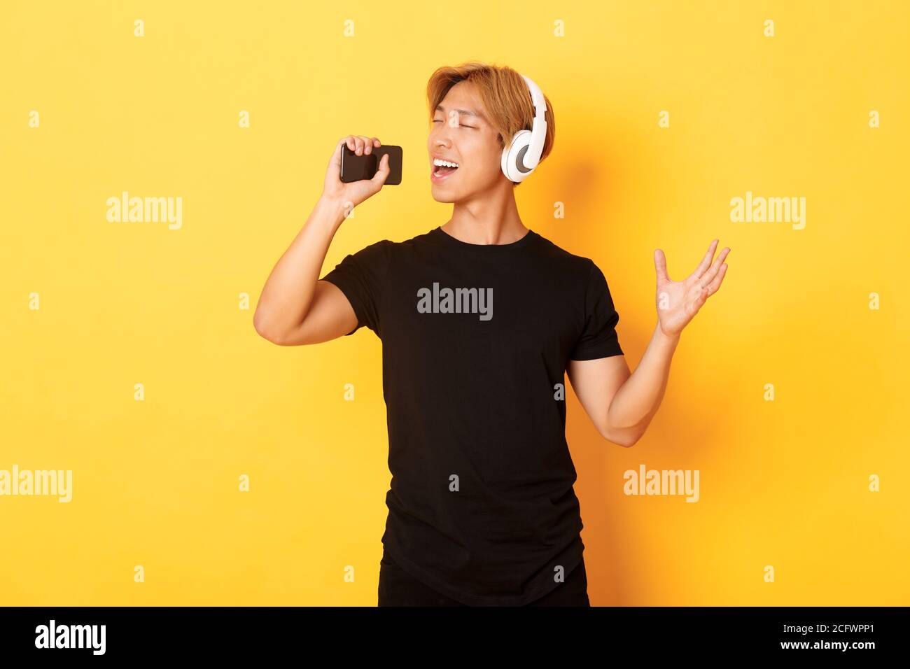 Joyful attractive korean guy in headphones, playing karaoke app