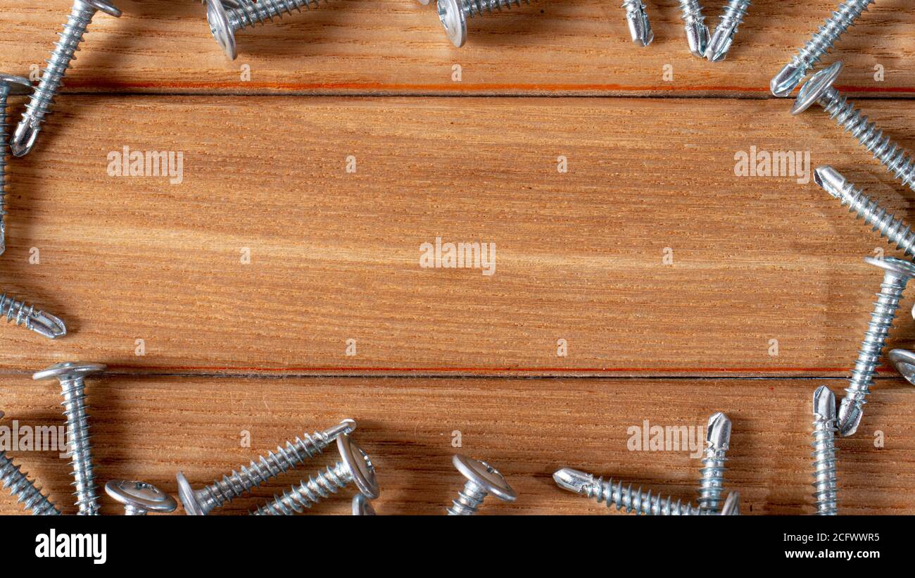 Self-cutters on a wood brown background banner with space for text. Construction tools, self-tapping screws for fastening. Black screw hardware. Stock Photo