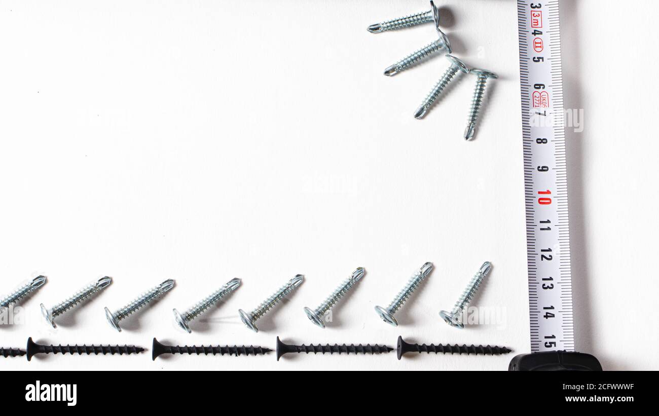 Self-tapping screw and measuring roulette on a white background banner with space for text. Construction tools, fastening hardware. Stock Photo
