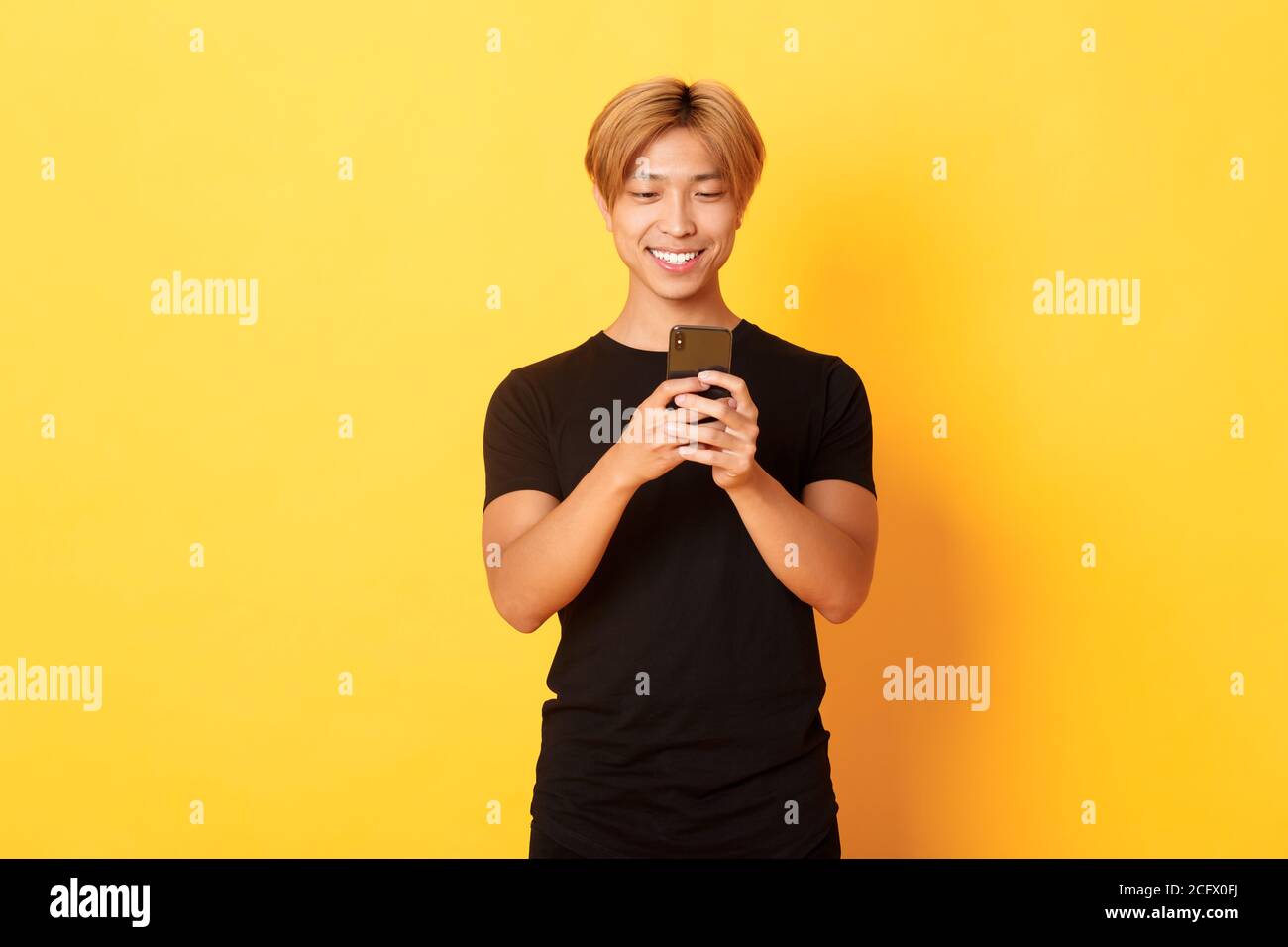 Portrait of handsome stylish asian guy with blond hair, using mobile ...