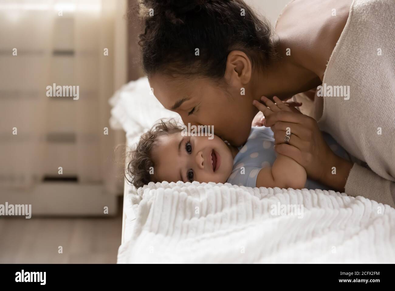 Affectionate african ethnicity mother kissing cheek of little toddler baby. Stock Photo