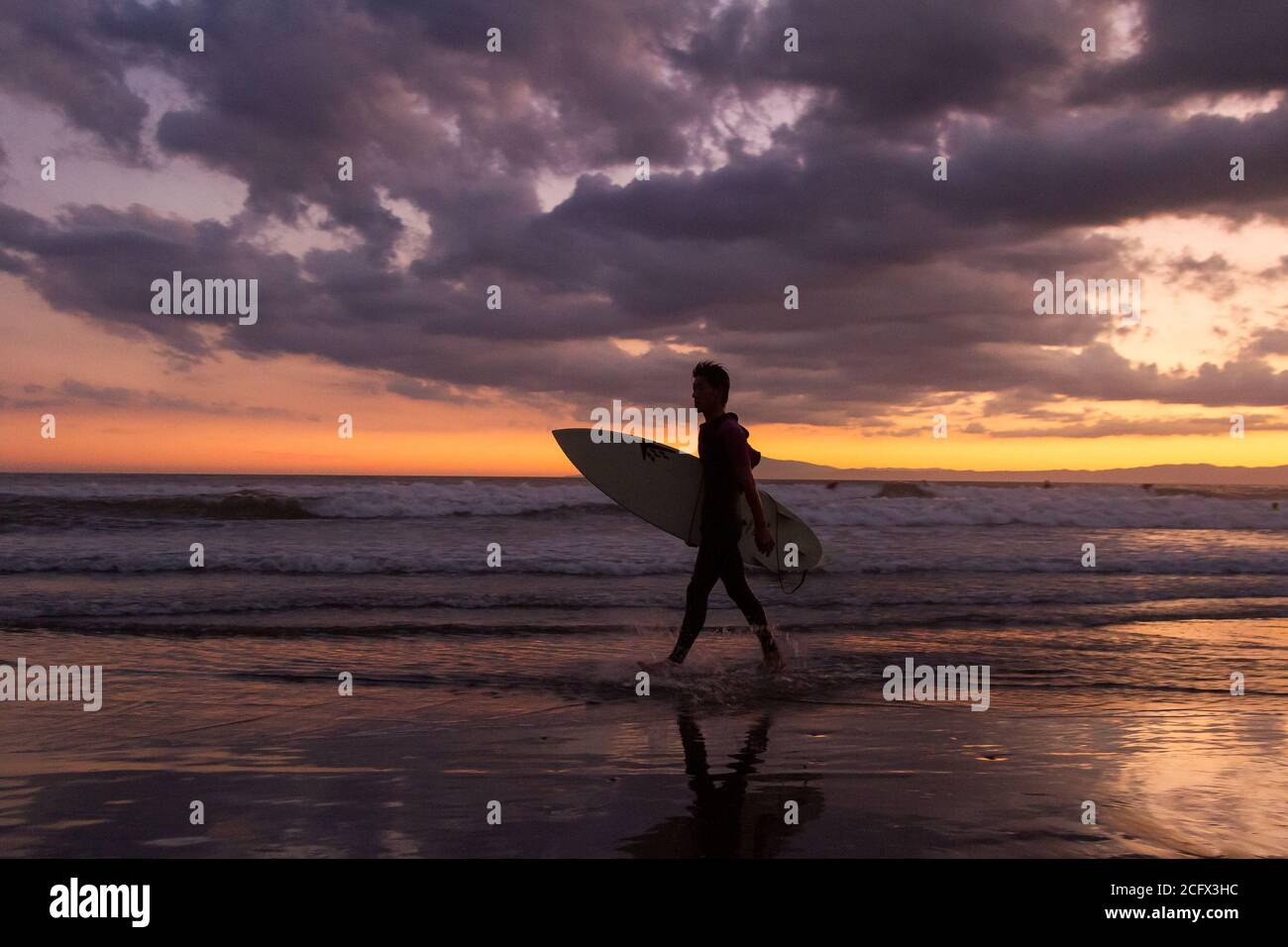 A surferscomes ashore  at sunset on a beach in Enoshima, Kanagawa, Japan. Stock Photo