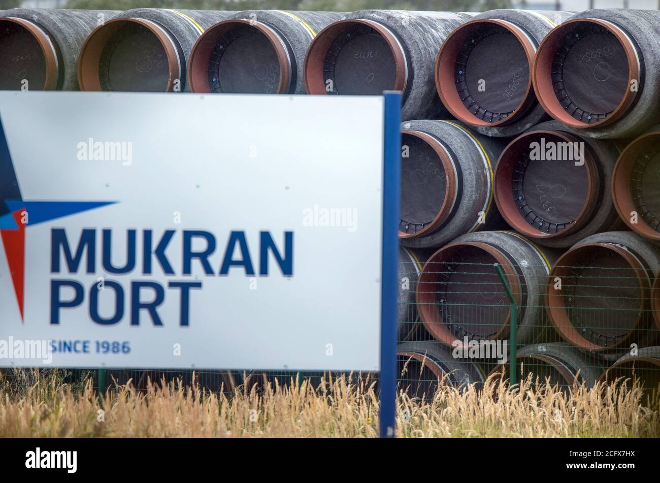 08 September 2020, Mecklenburg-Western Pomerania, Mukran: Pipes for the Nord Stream 2 natural gas pipeline are located behind a sign with the inscription 'Mukran Port' on a storage yard in the port of Mukran on the island of Rügen. Special ships are currently being prepared in the port for use in the further construction of the Nord Stream 2 Baltic Sea pipeline. Photo: Jens Büttner/dpa-Zentralbild/dpa Stock Photo