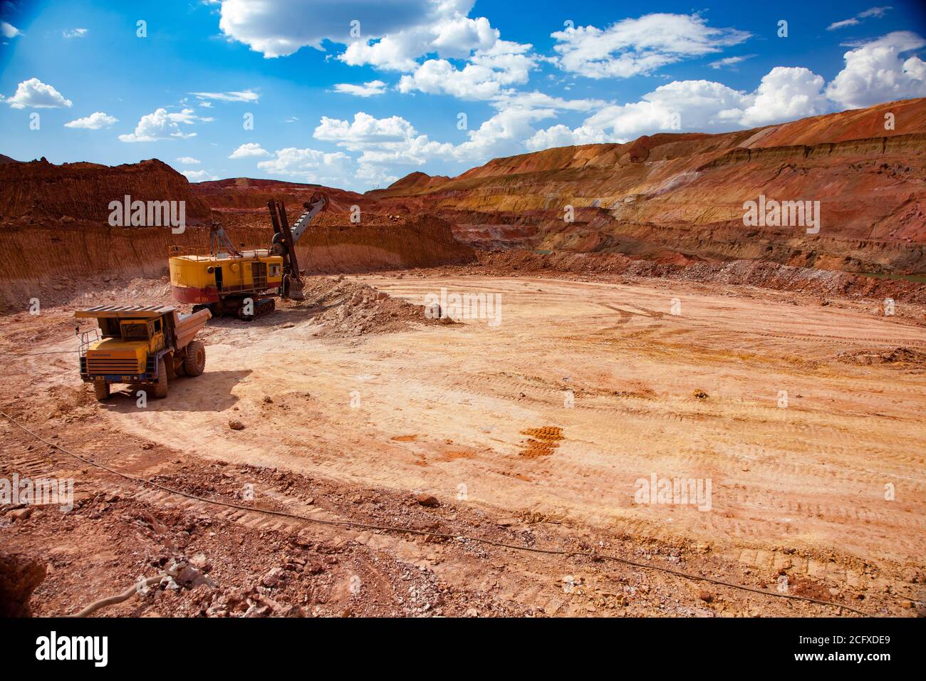 Aluminium ore mining and transporting. Bauxite clay quarry (mine). Excavator loading ore to Belaz dump truck. Blue sky with light clouds. Stock Photo