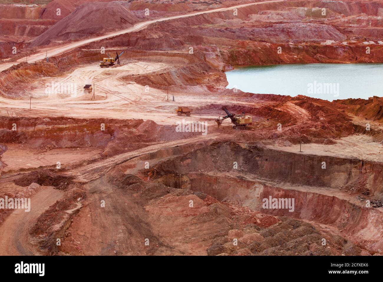 Aluminium ore quarry and blue lake in bauxite mine. Yellow excavators