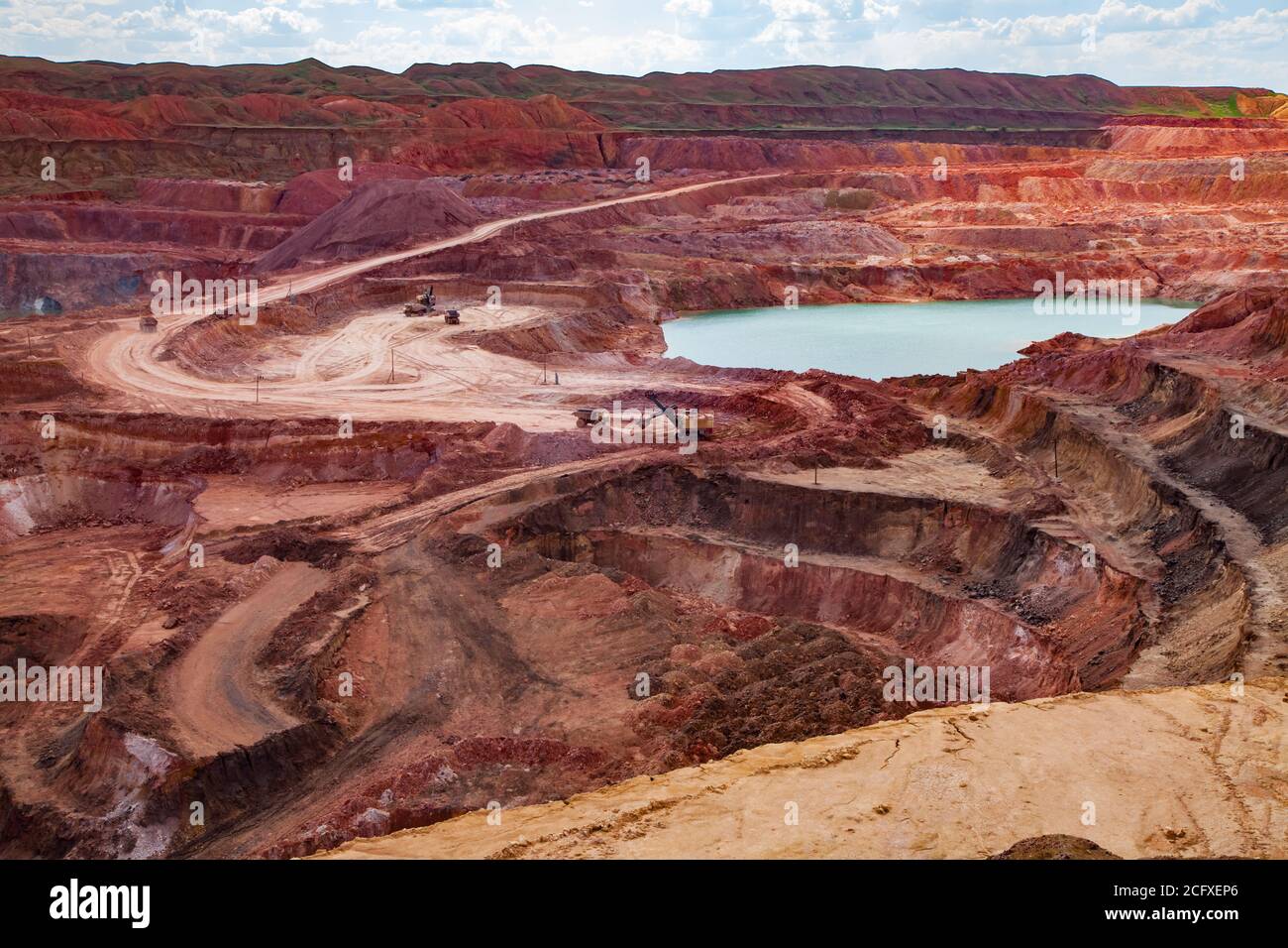 Aluminium ore quarry. Blue quarry lake in bauxite mine. Open cast (open-cut) mining. Against blue sky with clouds. Summer day. Stock Photo