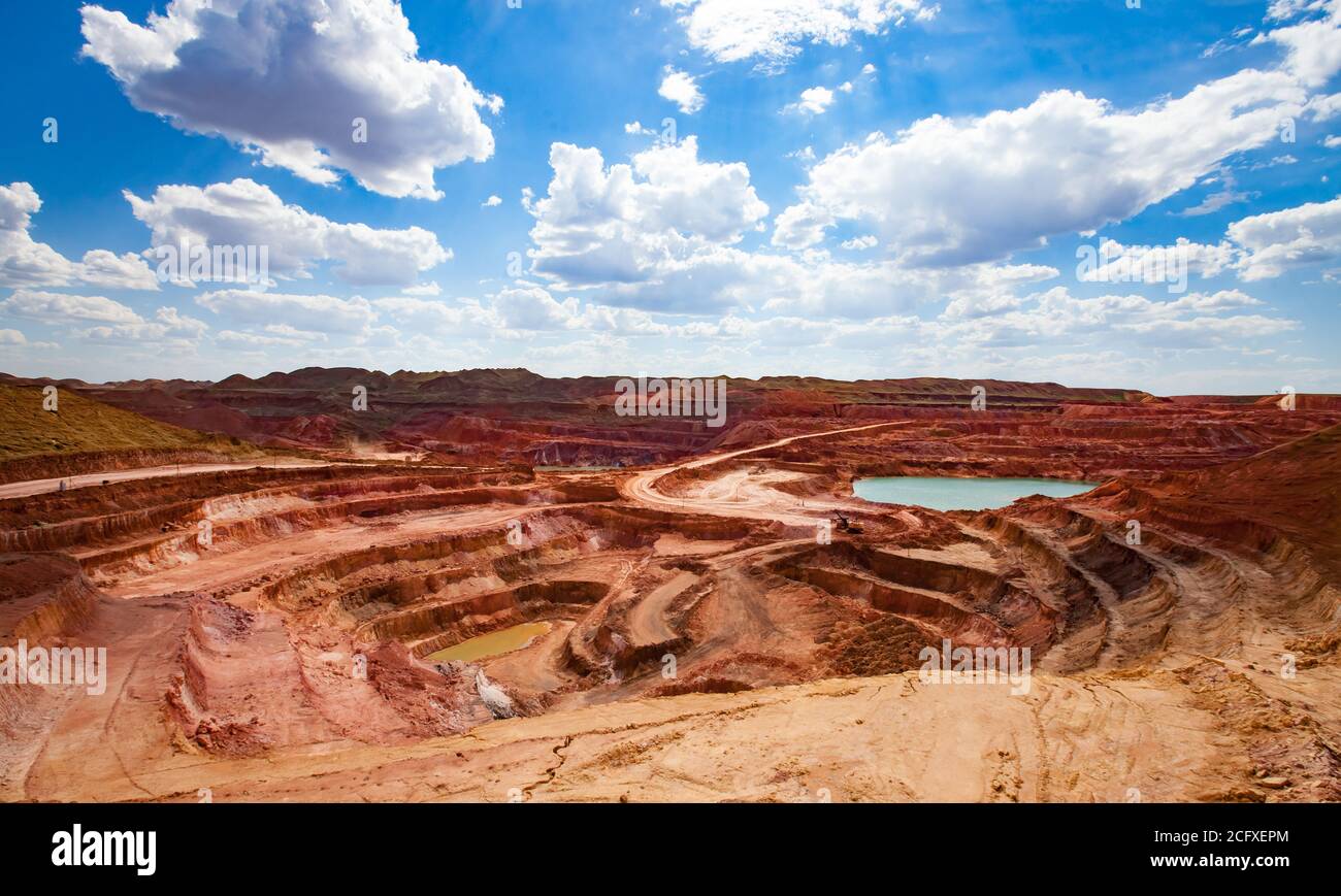 Aluminium ore quarry and blue lake in bauxite mine. Open cast (open-cut) mining. Panorama view. On blue sky with clouds in a summer day. Stock Photo