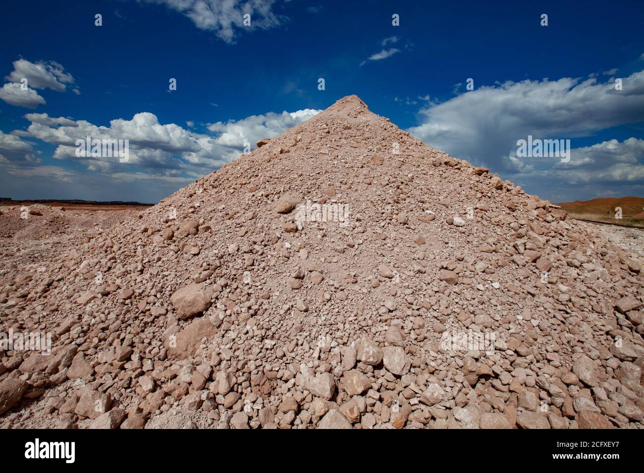 Pyramid heap of minerals. Aluminium ore mining. Bauxite clay quarry on blue sky with clouds. Stock Photo