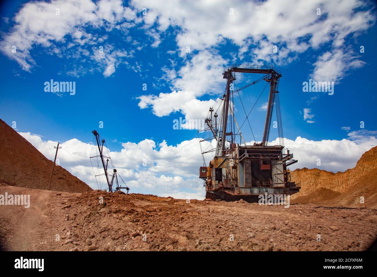 Aluminium ore quarry. Bauxite clay open-cut mining. Walking dragline excavators and empty rocks. On red and orange soil and blue sky with clouds. Stock Photo