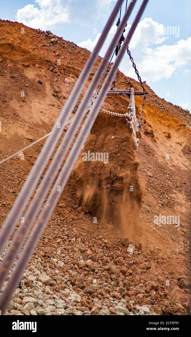 Aluminium ore quarry. Bauxite clay open-cut mining. Walking dragline excavator. Bucket with dusty ground. Stock Photo