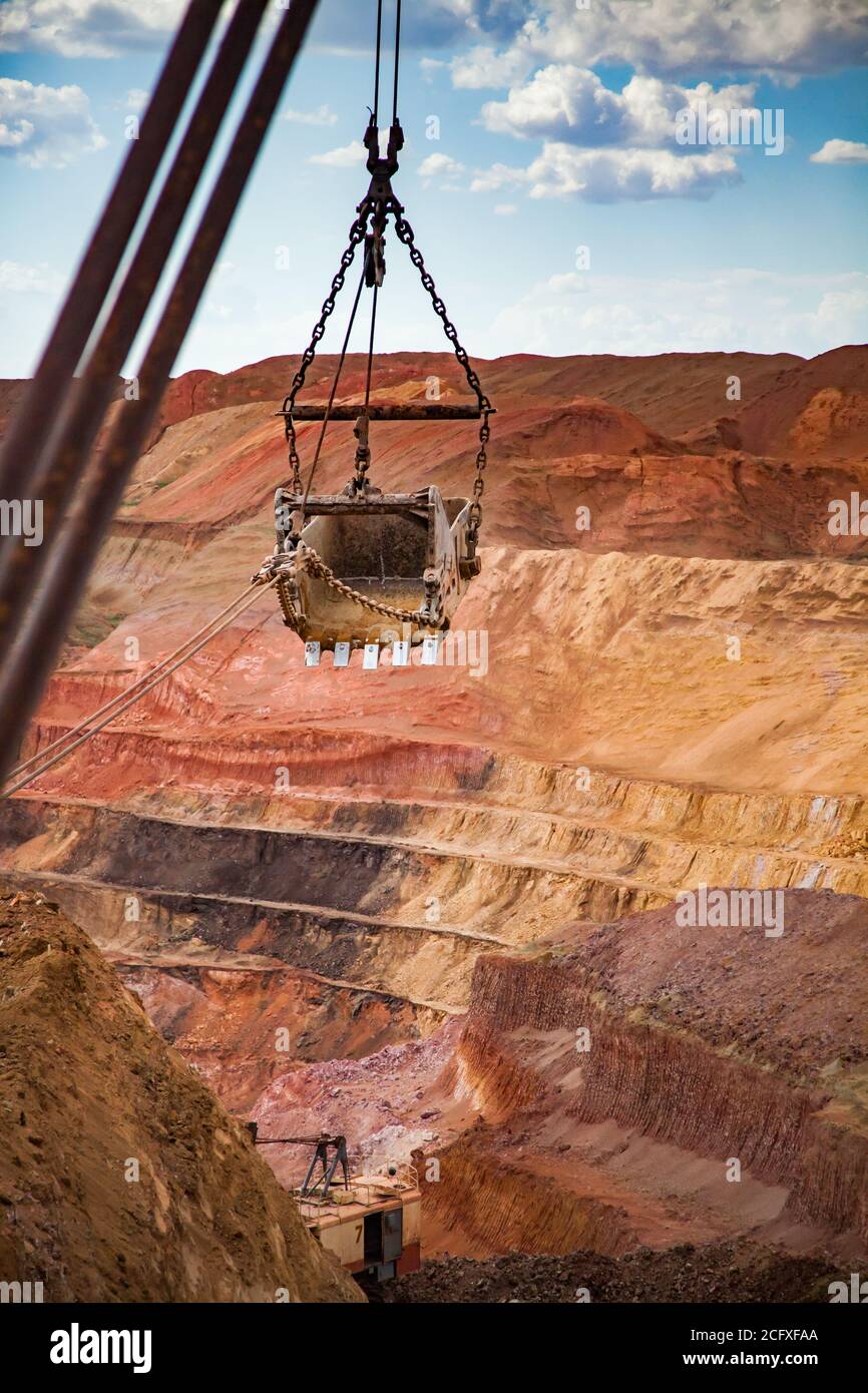 Aluminium ore quarry. Bauxite clay open-cut mining. Walking dragline excavator. bucket and small excavator down. Red soil and blue sky with clouds. Stock Photo