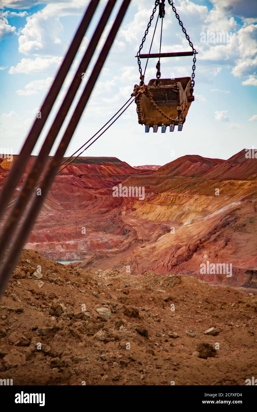 Aluminium ore quarry. Red bauxite clay open-cut mining. Walking dragline excavator bucket on cable of mast at work. Blue sky, clouds. Stock Photo