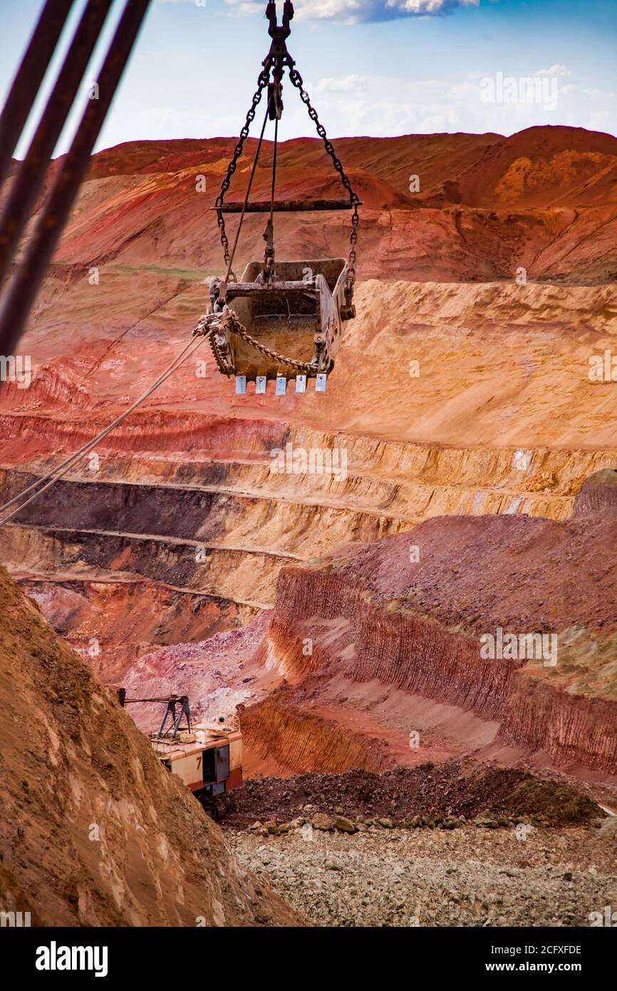Aluminium ore quarry. Red bauxite clay open-cut mining. Walking dragline excavator empty bucket on cable. Blue sky, clouds. Focus on foreground. Stock Photo