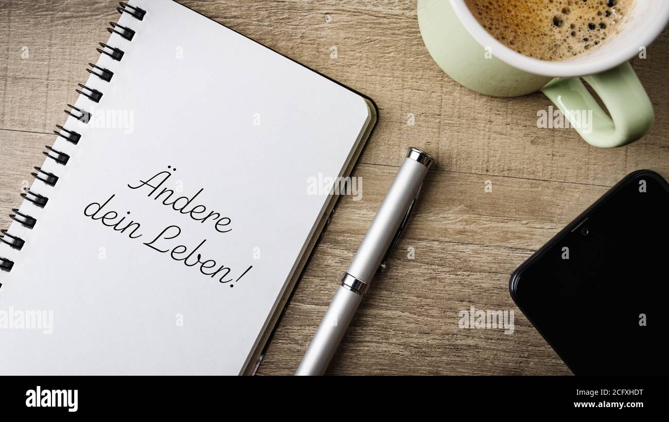 Flat lay. Work area with notepad, pen, cell phone and a cup of coffee. German Text. Translation: Change your life! Stock Photo