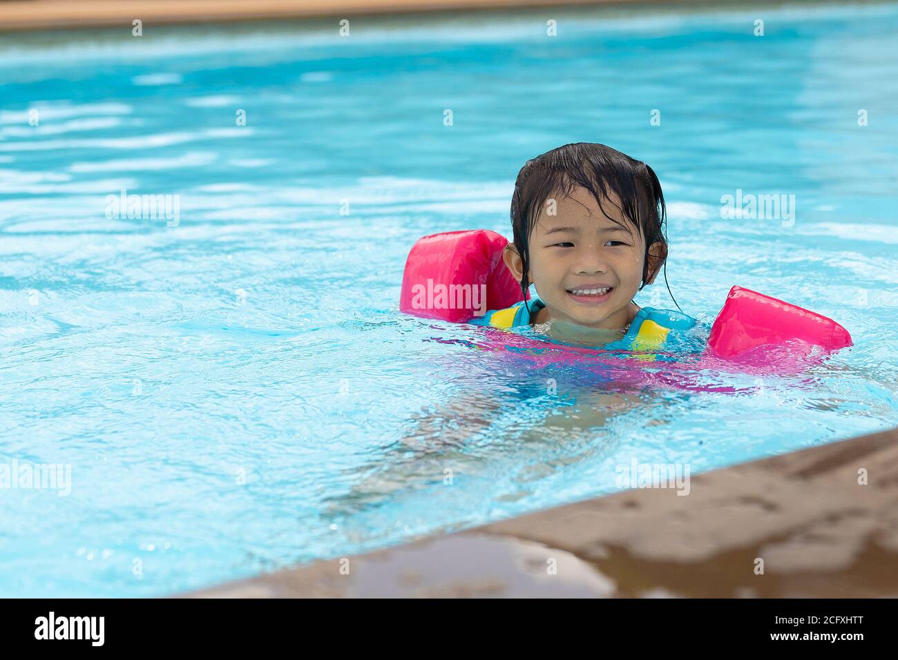 Asian cute little toddler girl in a colorful swimming suit relaxing in a pool having fun during summer vacation in a tropical resort. Stock Photo