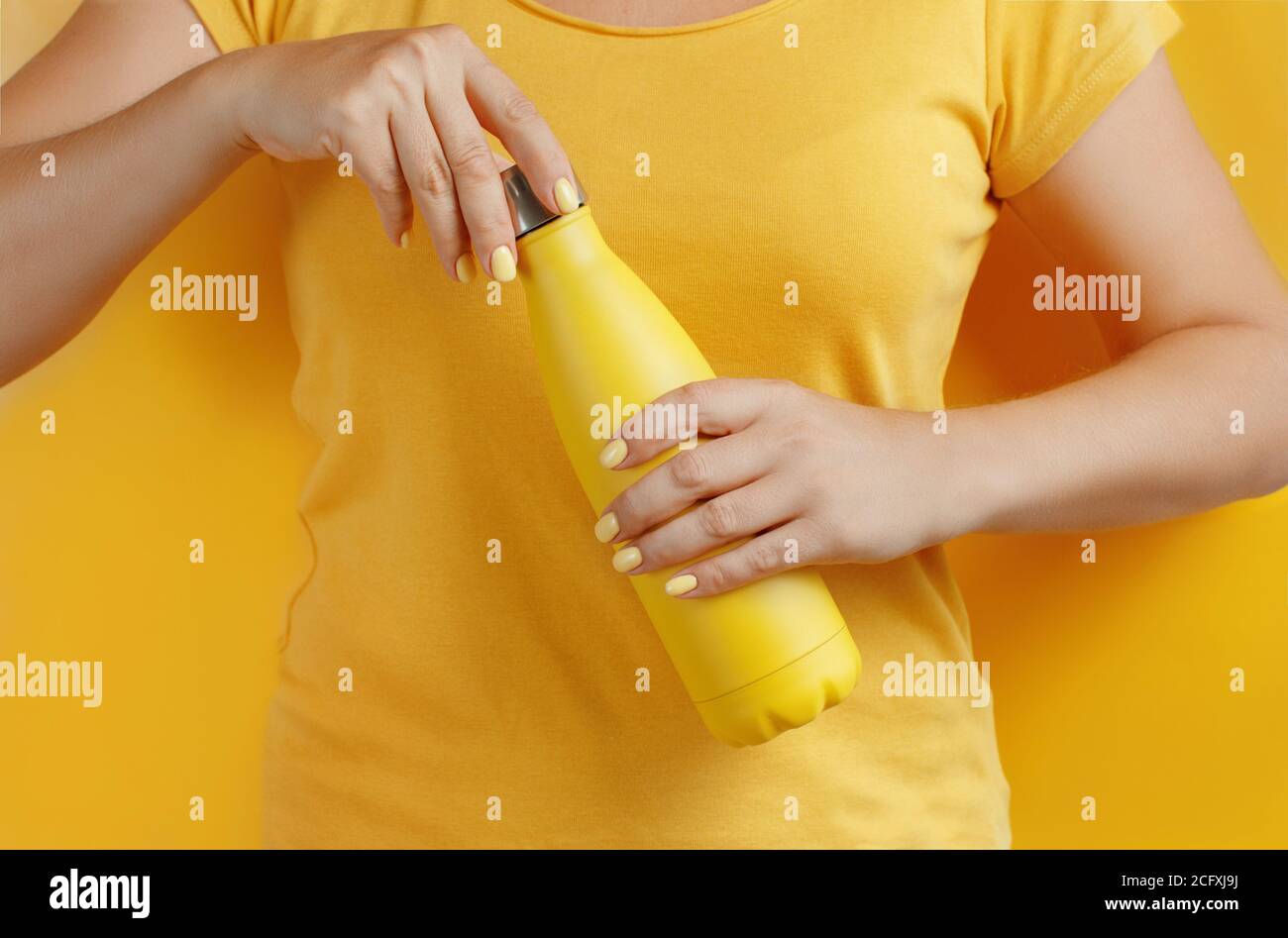 Close up of woman holding yellow reusable bottle on yellow  background Stock Photo