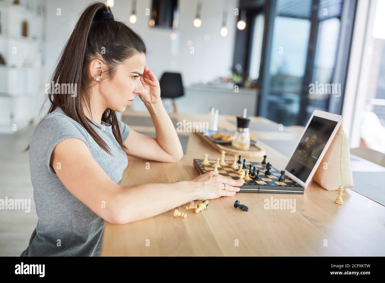 Woman playing chess at home thinks concentrated in video chat online Stock Photo