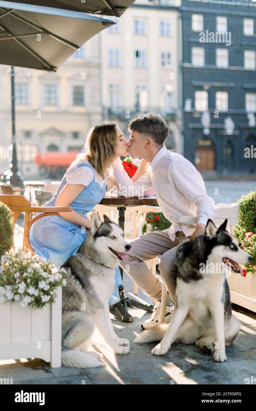 https://c8.alamy.com/comp/2CFXMFG/beautiful-young-couple-in-love-enjoying-summer-walk-in-the-city-street-with-their-husky-dogs-sitting-at-the-table-in-cafe-outdoors-and-kissing-2CFXMFG.jpg