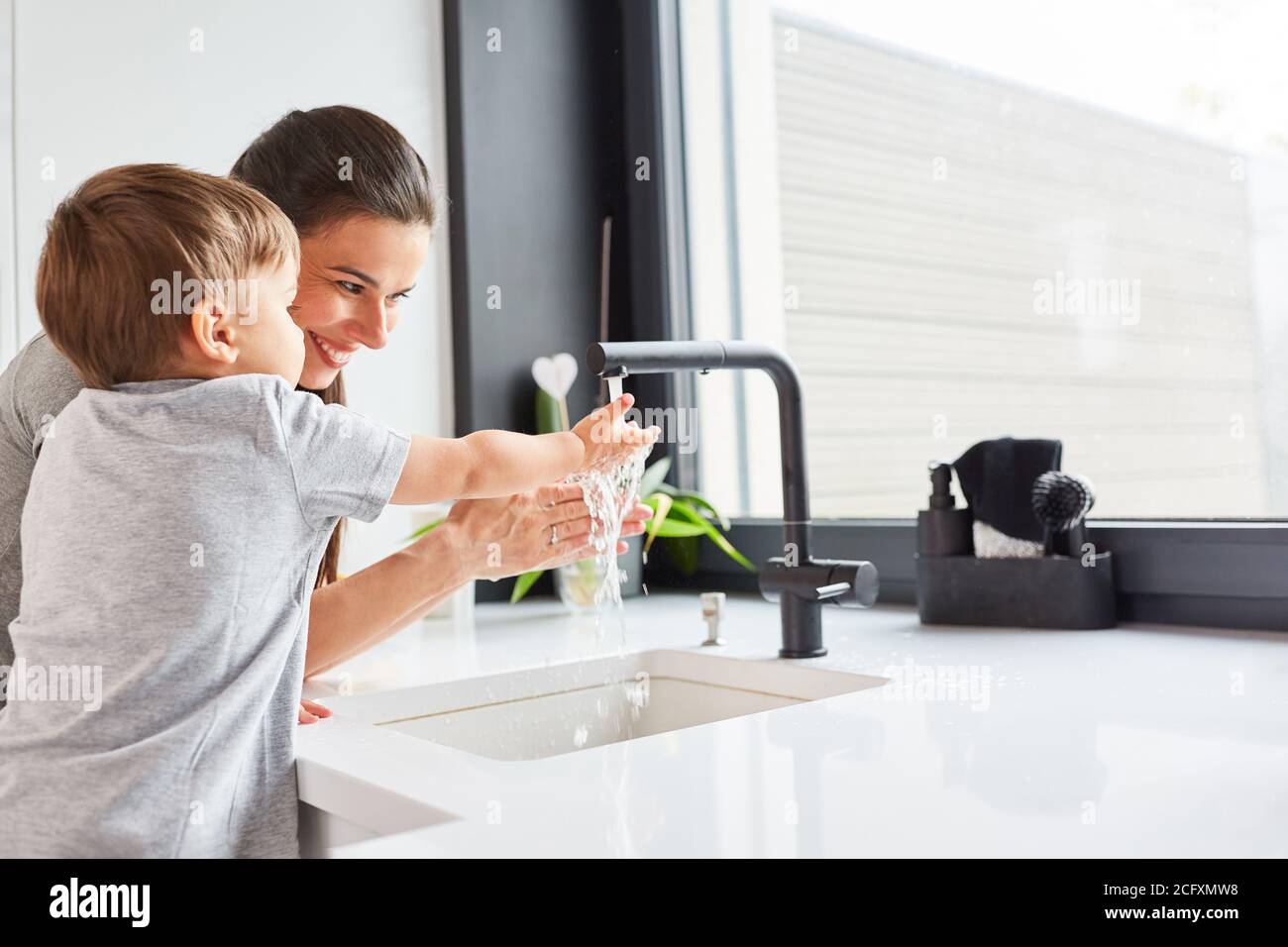 Mother helps child wash hands with soap as hygiene against Covid-19 Stock Photo