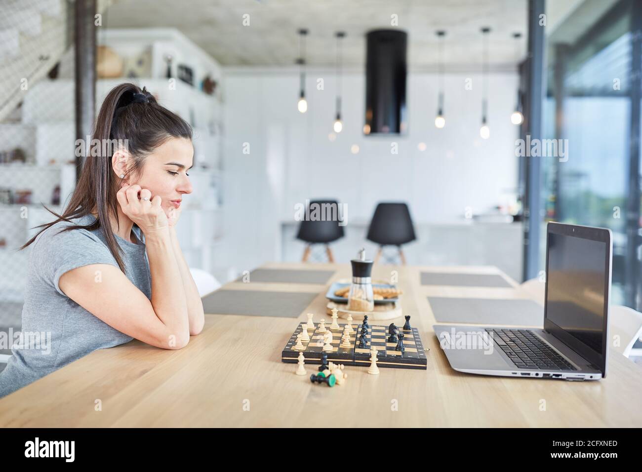 Woman at home playing chess on laptop computer thinking about video chat online Stock Photo