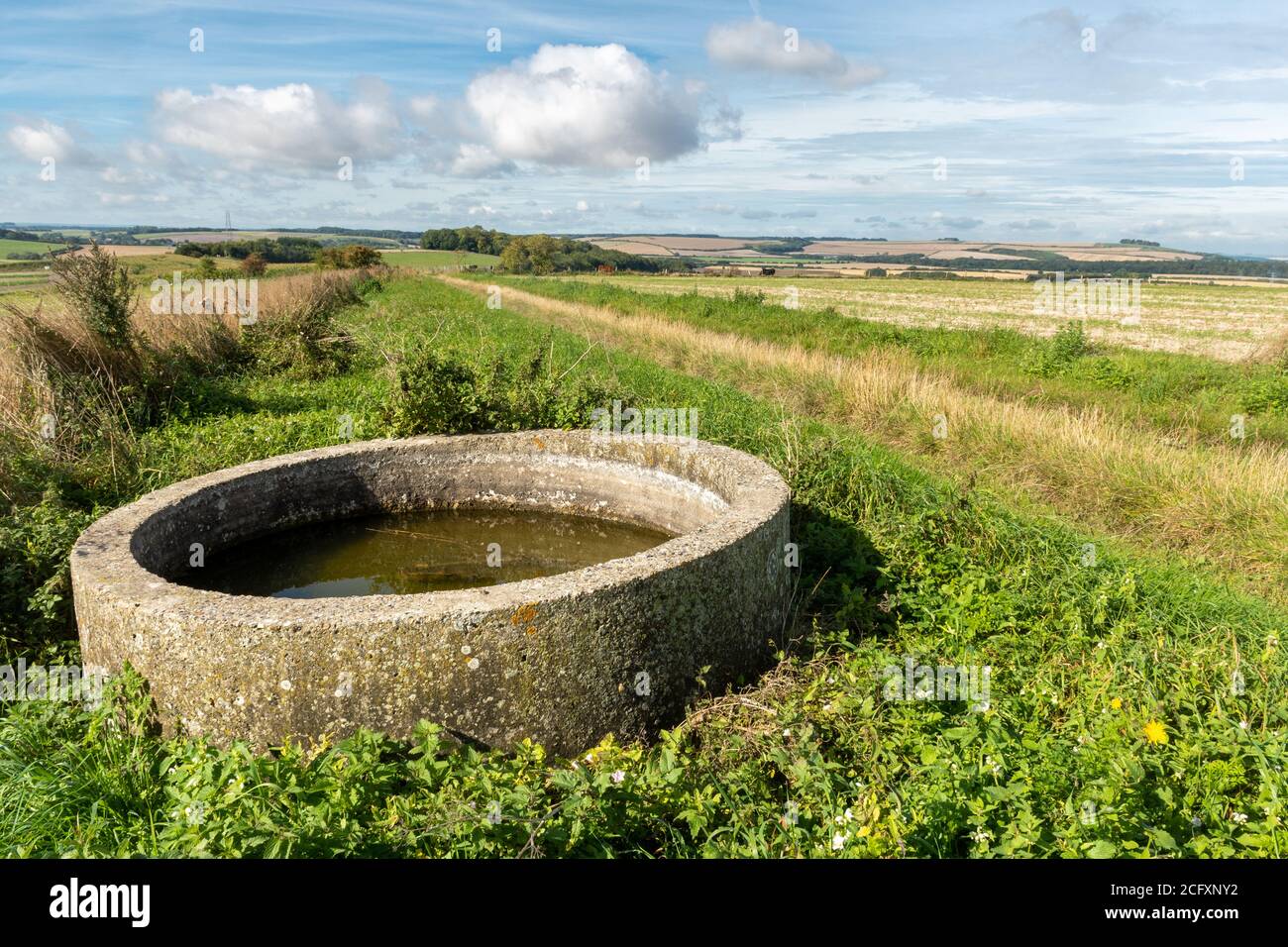 Countryside farmland landscape in the North Wessex Downs AONB near Wexcombe, Wiltshire, UK, with an unusual circular water trough in the foreground Stock Photo