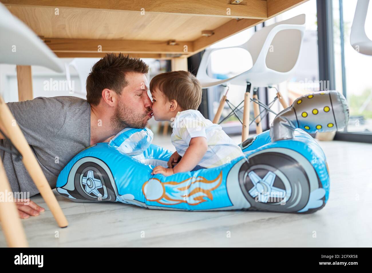 Father gives his son a kiss in the child's car while playing in the living room Stock Photo