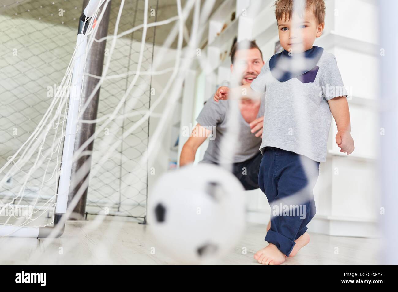 Toddler playing soccer scores a goal together with father in the living