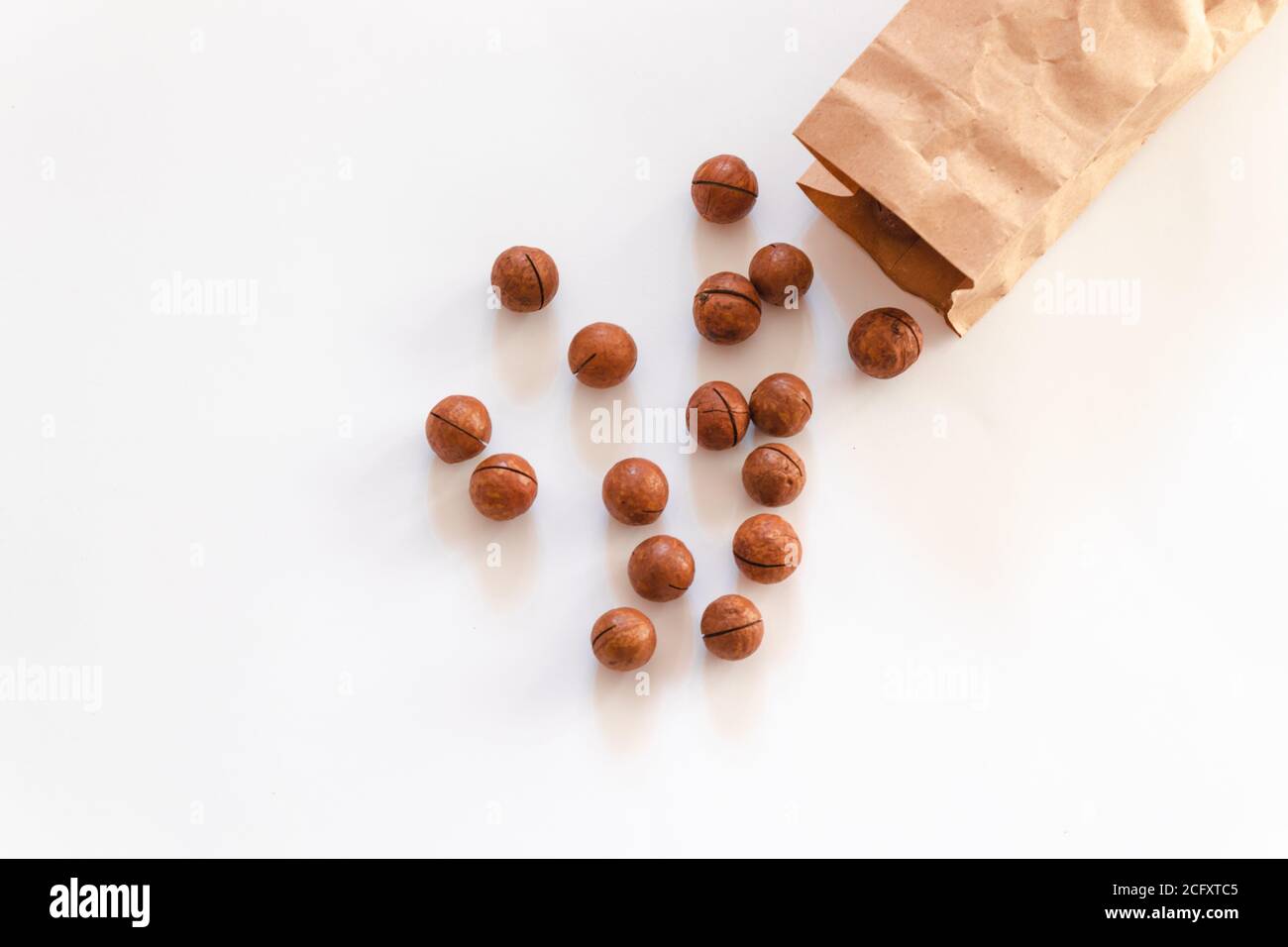Flat composition with macadamia nuts scattered from paper bag on a white table Stock Photo