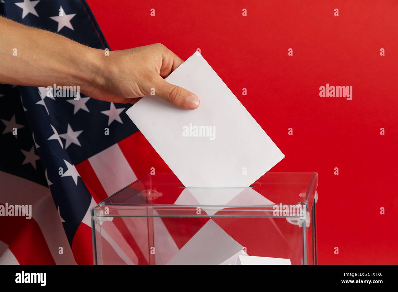 Man putting ballot into voting box on red background with american flag ...