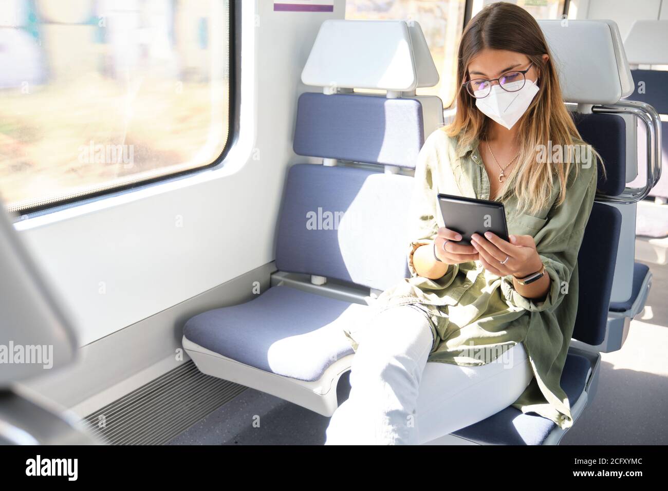 Young woman wearing face mask and reading a e-book in the train. New normal travel concept. Stock Photo